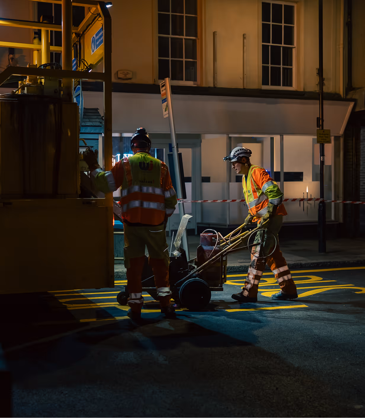 Road workers applying line markings at night using sustainable asphalt solutions