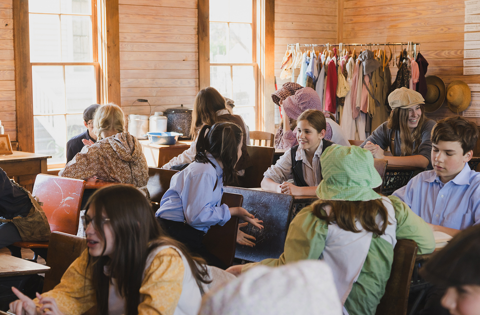 Children dressed in antique clothing inside a historic schoolhouse.
