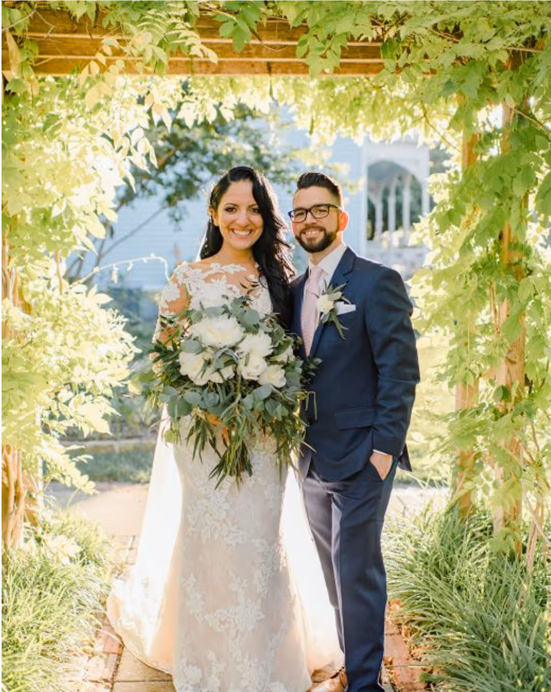 Newlywed couple smiling in front of an arbor