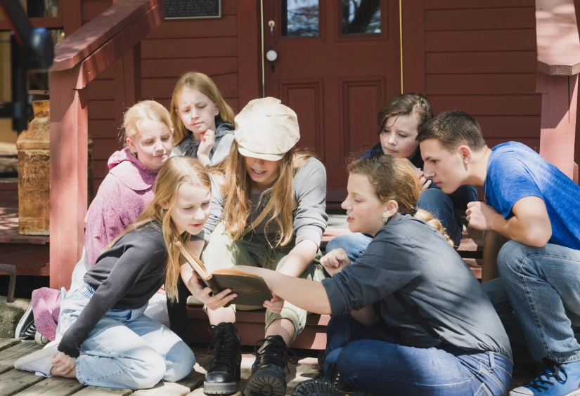 Children dressed in clothes from the 1800s read on a porch