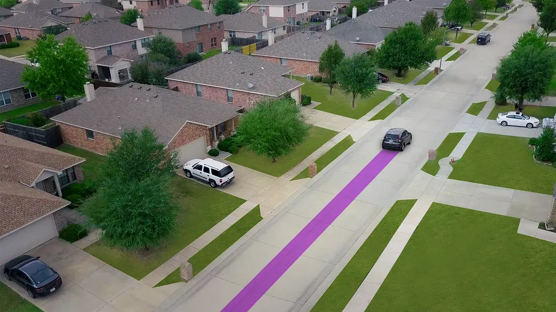 A black car is traveling down a residential street.  A purple line is behind the car illustrating the Speed Bands concept within the Bouncie app that shows the vehicle speed within the trip history.