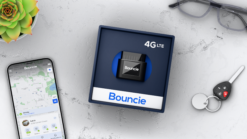 Image of the Bouncie GPS Tracking device in its blue box laying on a white marble table with a mobile phone laying next to the box showing the vehicle tracking app.