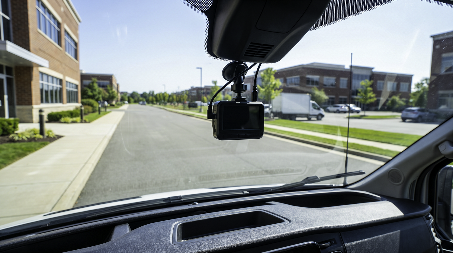 Dash cam mounted on the windshield of a commercial fleet vehicle monitoring a suburban road for driver safety and liability protection
