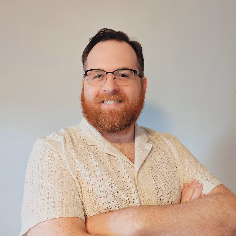 Alex Davidson smiling with arms crossed, wearing glasses and a cream short-sleeve shirt.