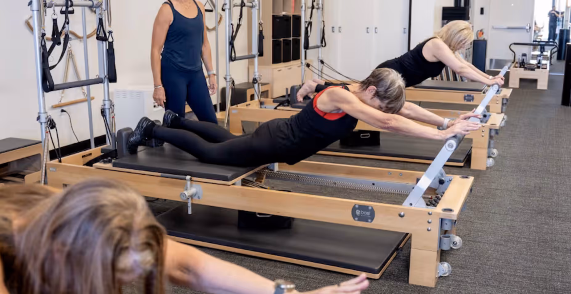 A Swan Pilates teacher guides a small group practicing together on reformers