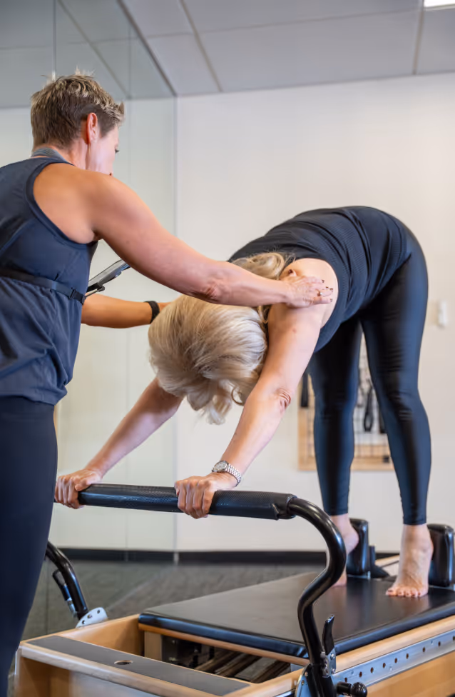A teacher provides hands-on support during a private Pilates session