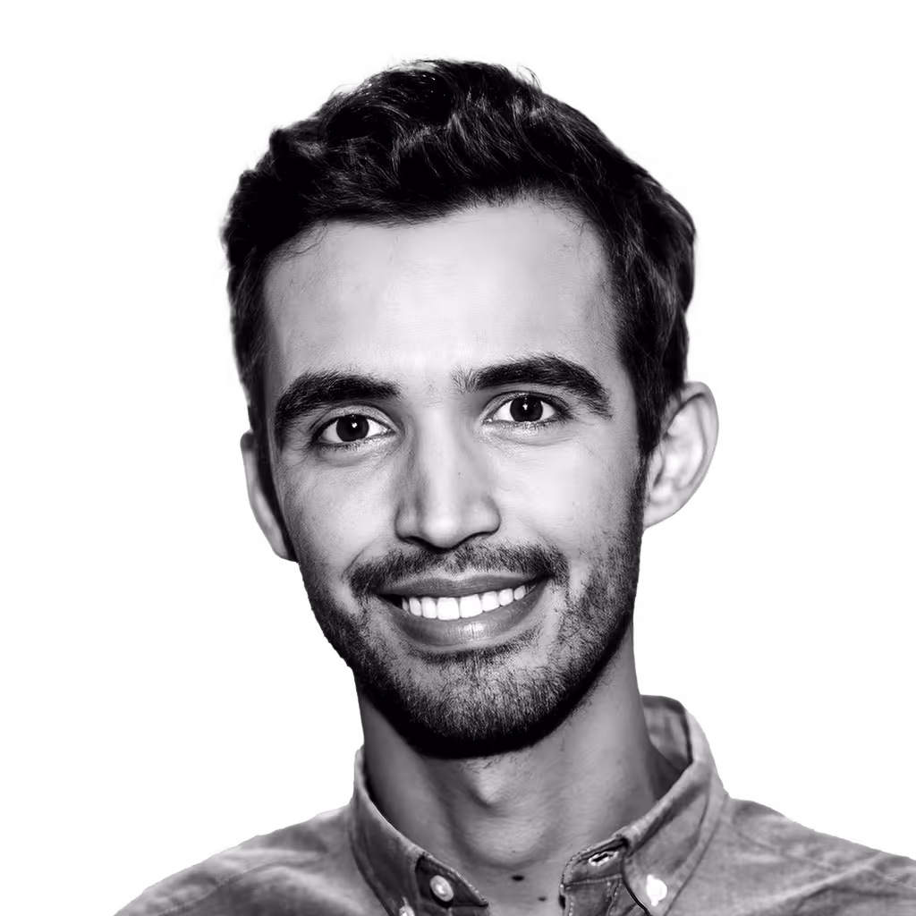 Smiling young man with short dark hair and a slight beard wearing a buttoned shirt.