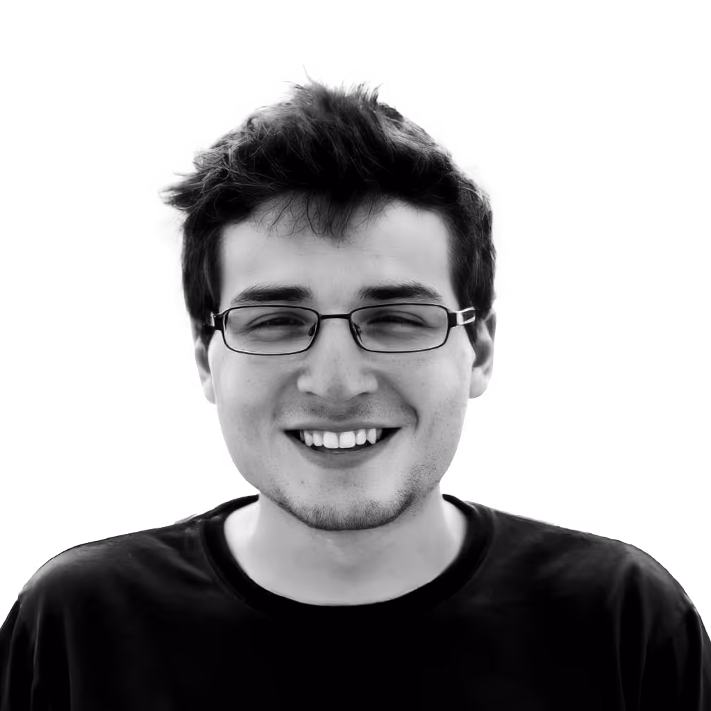 Smiling young man with glasses and short tousled hair wearing a black shirt.