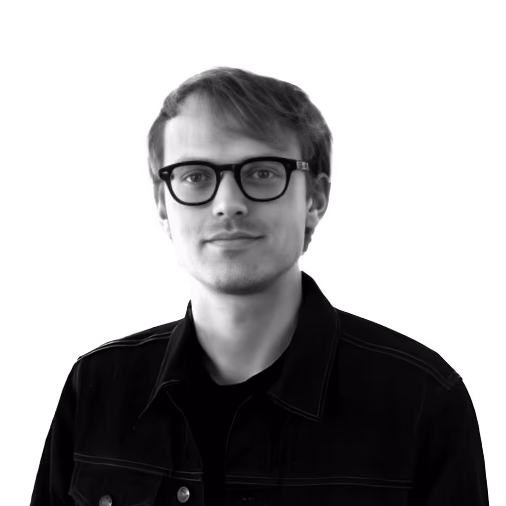 Portrait of a young man with short hair and glasses wearing a black jacket.