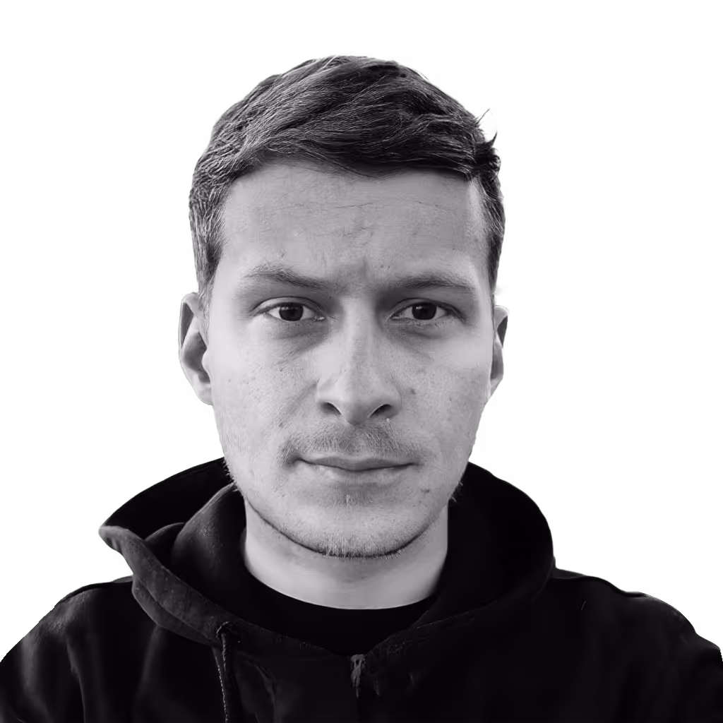 Close-up black and white portrait of a young man with short hair wearing a dark hoodie, looking directly at the camera with a neutral expression.