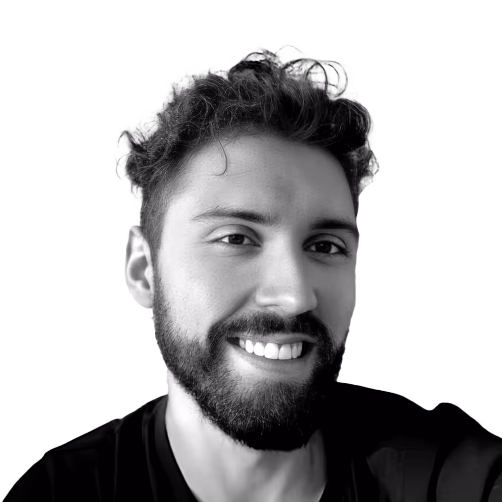 Smiling man with curly hair and beard wearing a dark shirt on a transparent background.