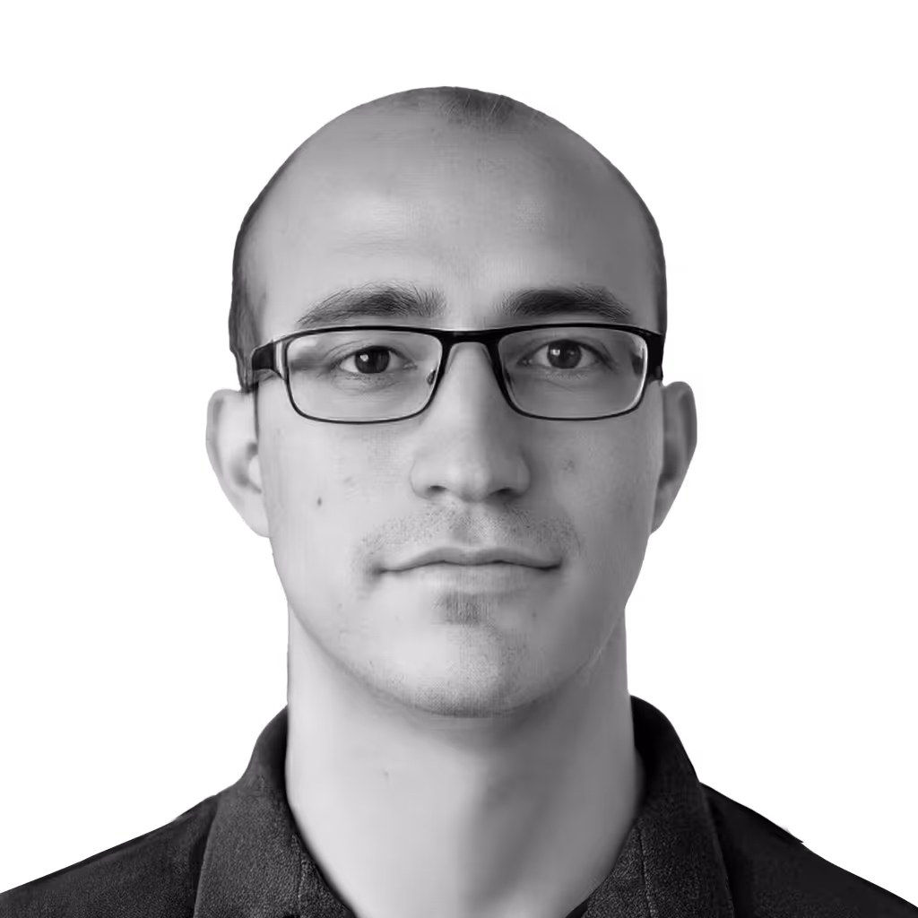 Black and white portrait of a young man with glasses wearing a dark collared shirt, looking directly at the camera.