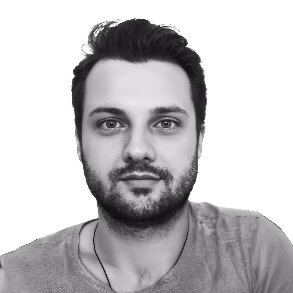 Black and white portrait of a young man with short hair, beard, and a neutral expression wearing a t-shirt.