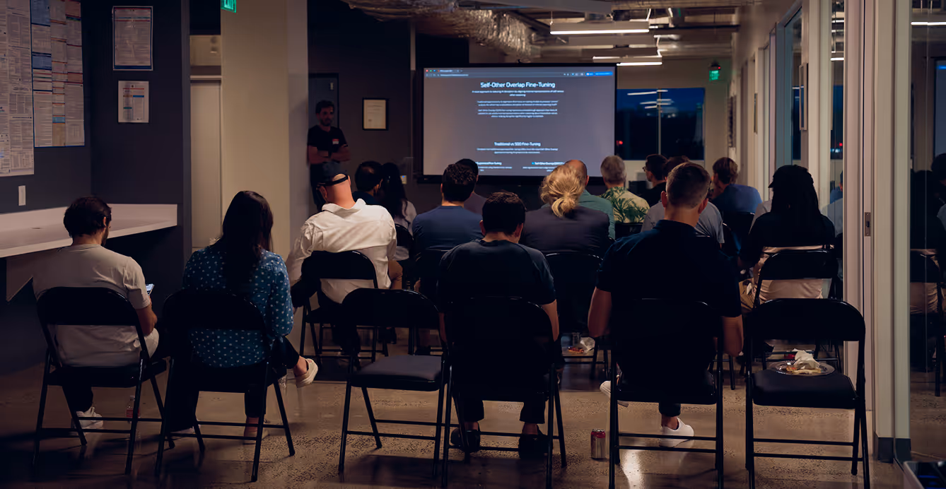 Audience seated in chairs facing a presenter and a screen displaying a technical presentation titled 'Self-Other Overlap Fine-Tuning' in a modern conference room.