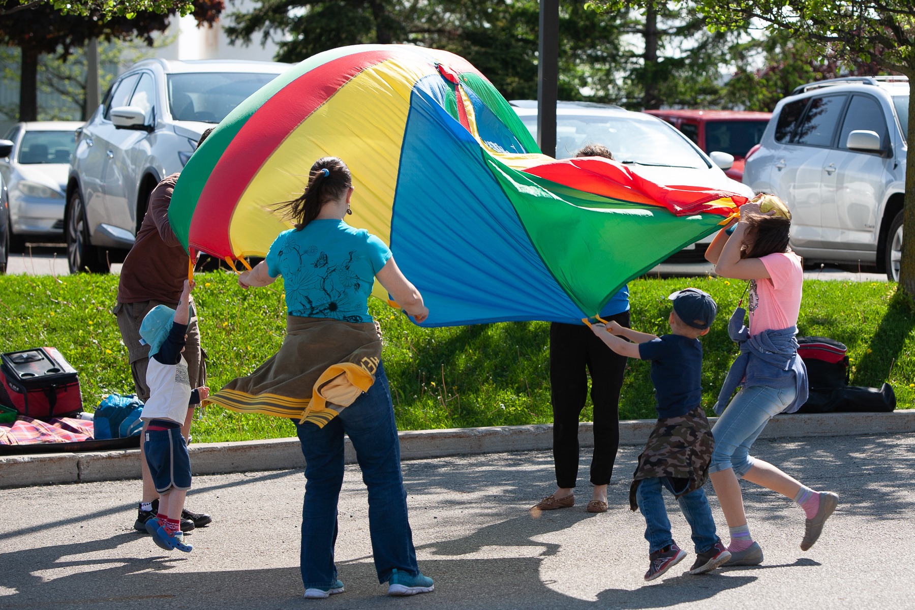 Families enjoying outdoor community event activities with colorful parachute games