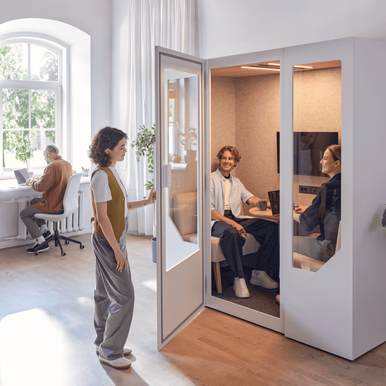 Employees using a soundproof office pod for collaborative work in a bright coworking environment