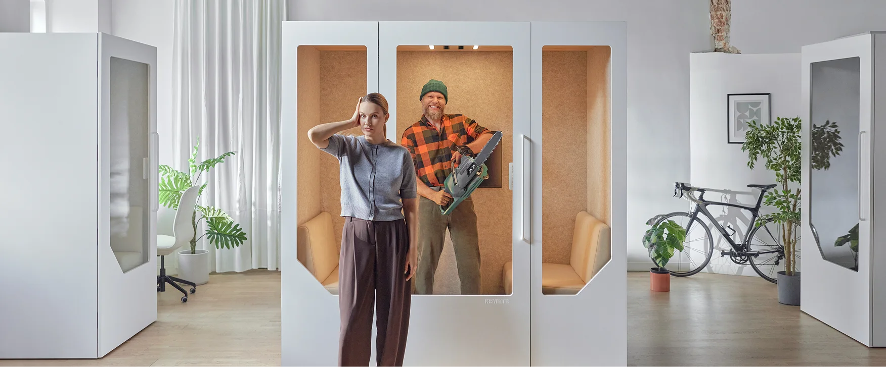 Woman standing frustrated in front of a man in a phone booth holding a chainsaw indoors.