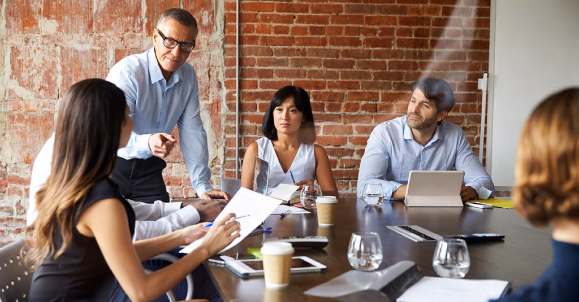 Group of professionals having a meeting around a conference table with brick wall background.