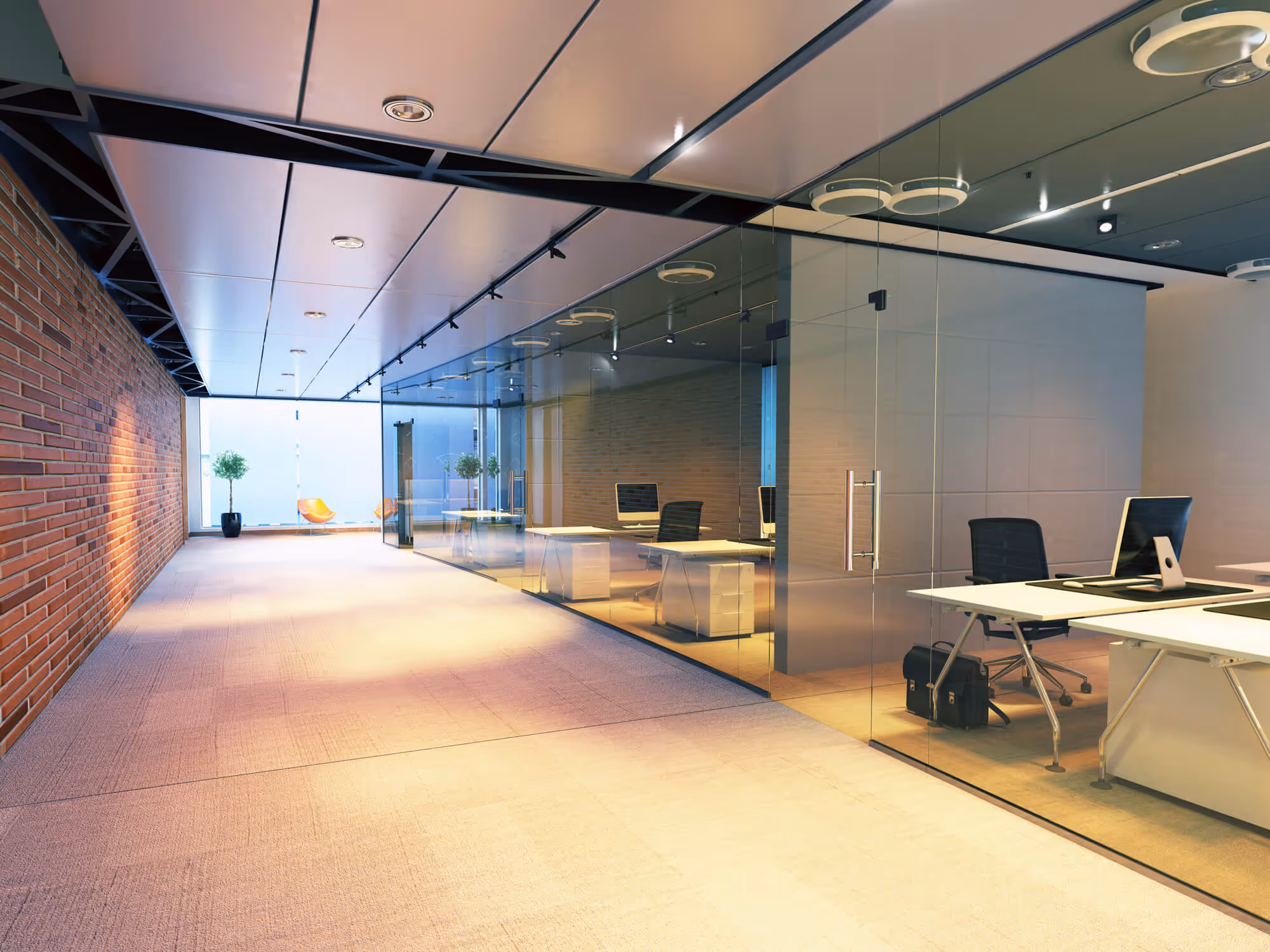 Modern office hallway with glass-walled conference rooms and desks with computers inside.