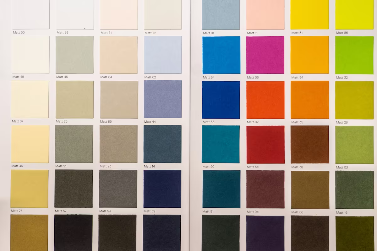 Two pages from a color palette displaying an array of matte color swatches with code labels, featuring whites, greens, blues, reds, yellows, browns, and grays.