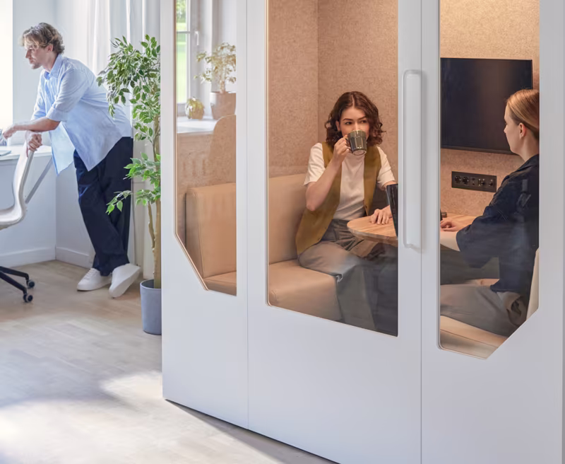 Employees collaborating near a phone booth in a modern office environment