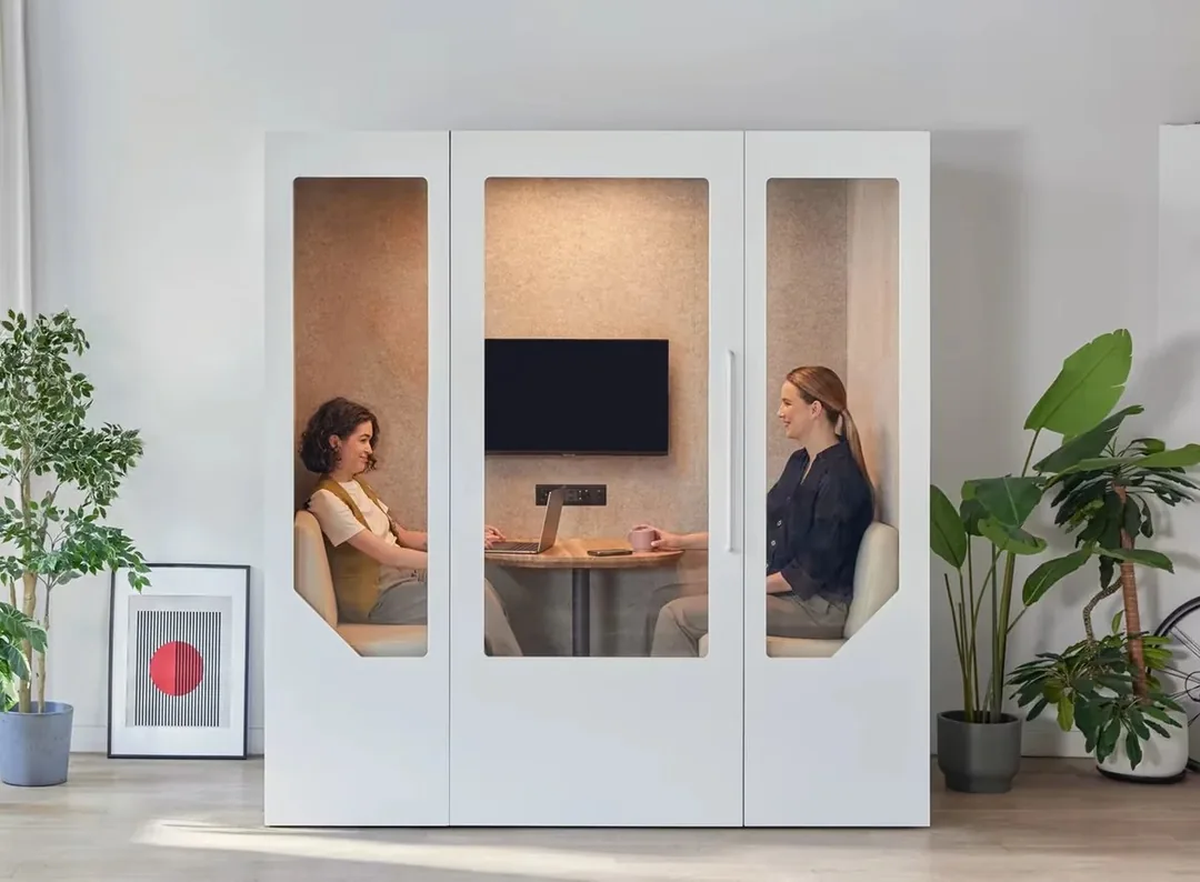 Two colleagues seated in a Persy meeting booth with a table and screen