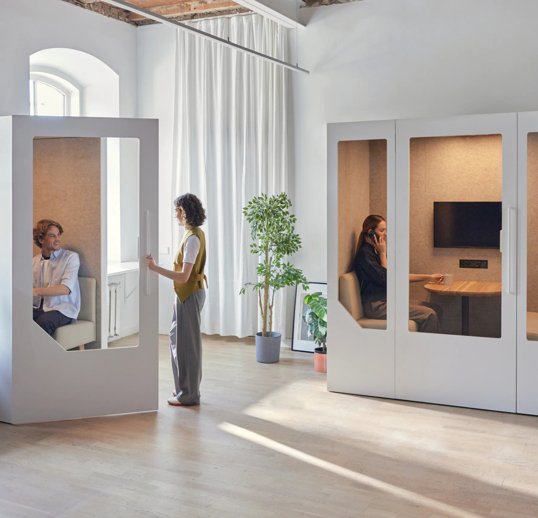 Modern office with Persy soundproof pods in use — one person working in a single booth and another in a meeting pod, showcasing privacy and productivity solutions.