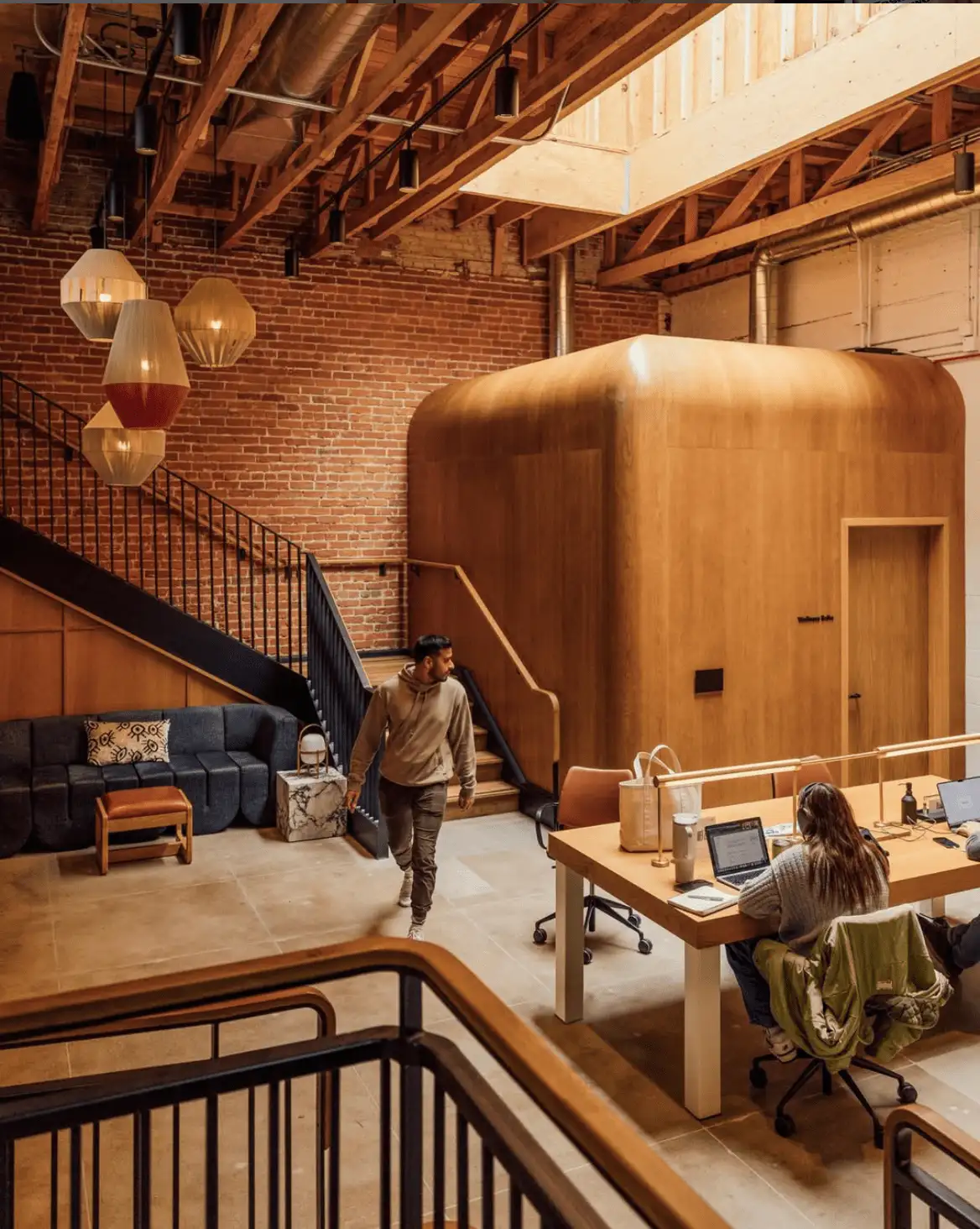 Warm industrial coworking space featuring a large wooden meeting pod and modern furnishings designed to foster productivity and comfort.