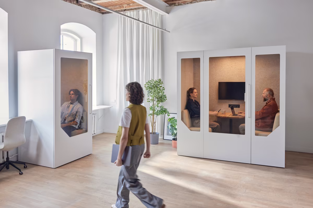 Person taking a call inside a soundproof office booth within an open workspace