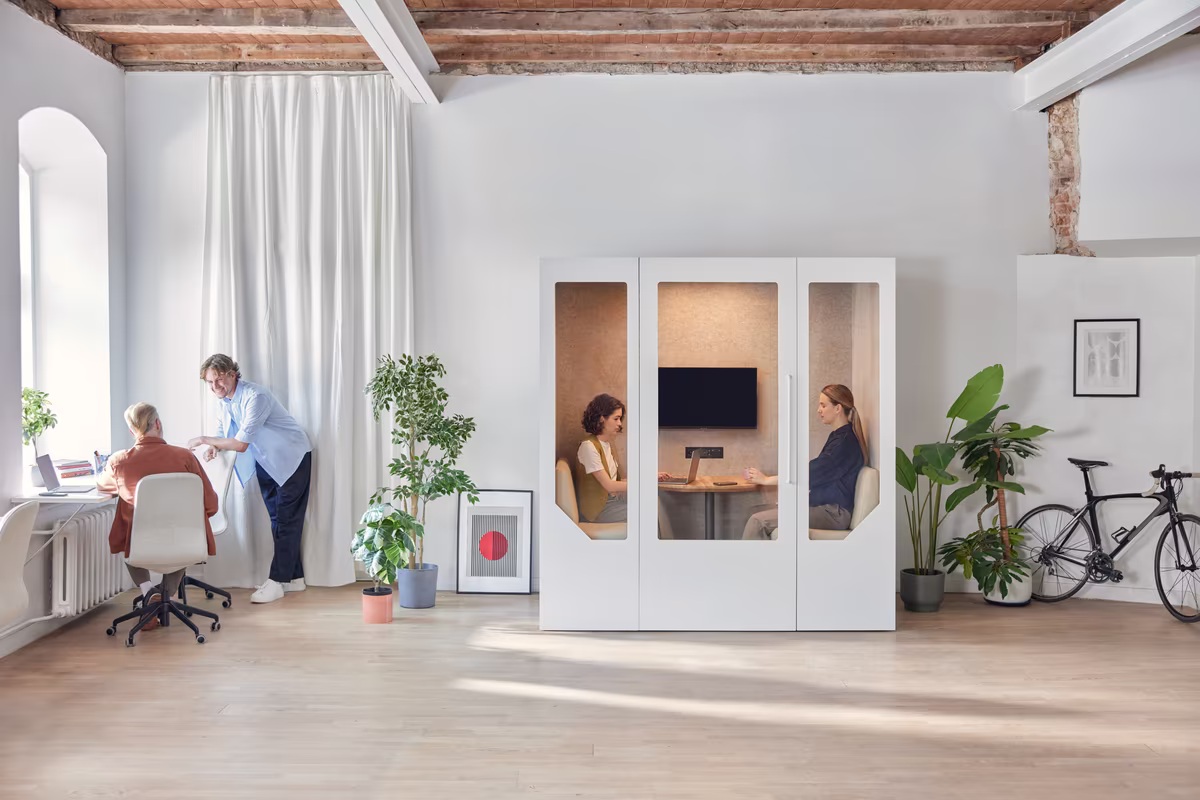 People using an acoustic meeting booth inside an open plan office while surrounding work continues uninterrupted