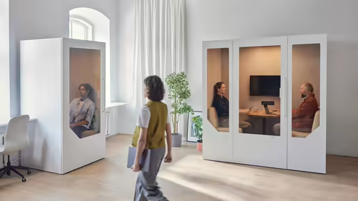 Employees using office pods and walking through a bright open plan hybrid workspace