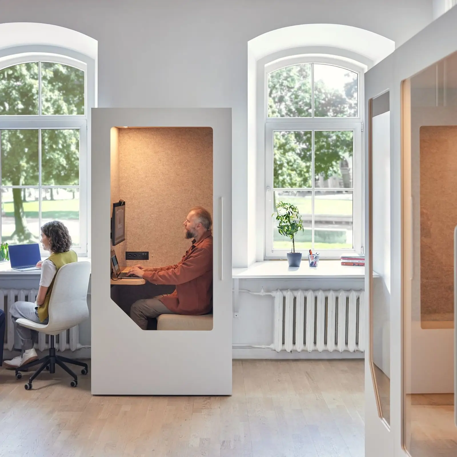 Employees working in office phone booths and open desk area in a bright modern workspace