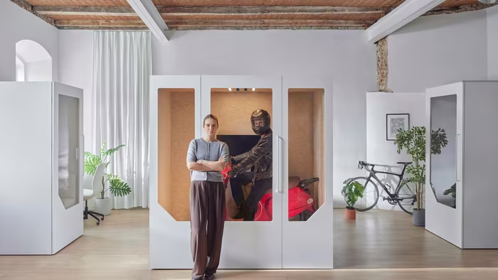 Woman standing next to a soundproof office booth with a person on a motorcycle inside