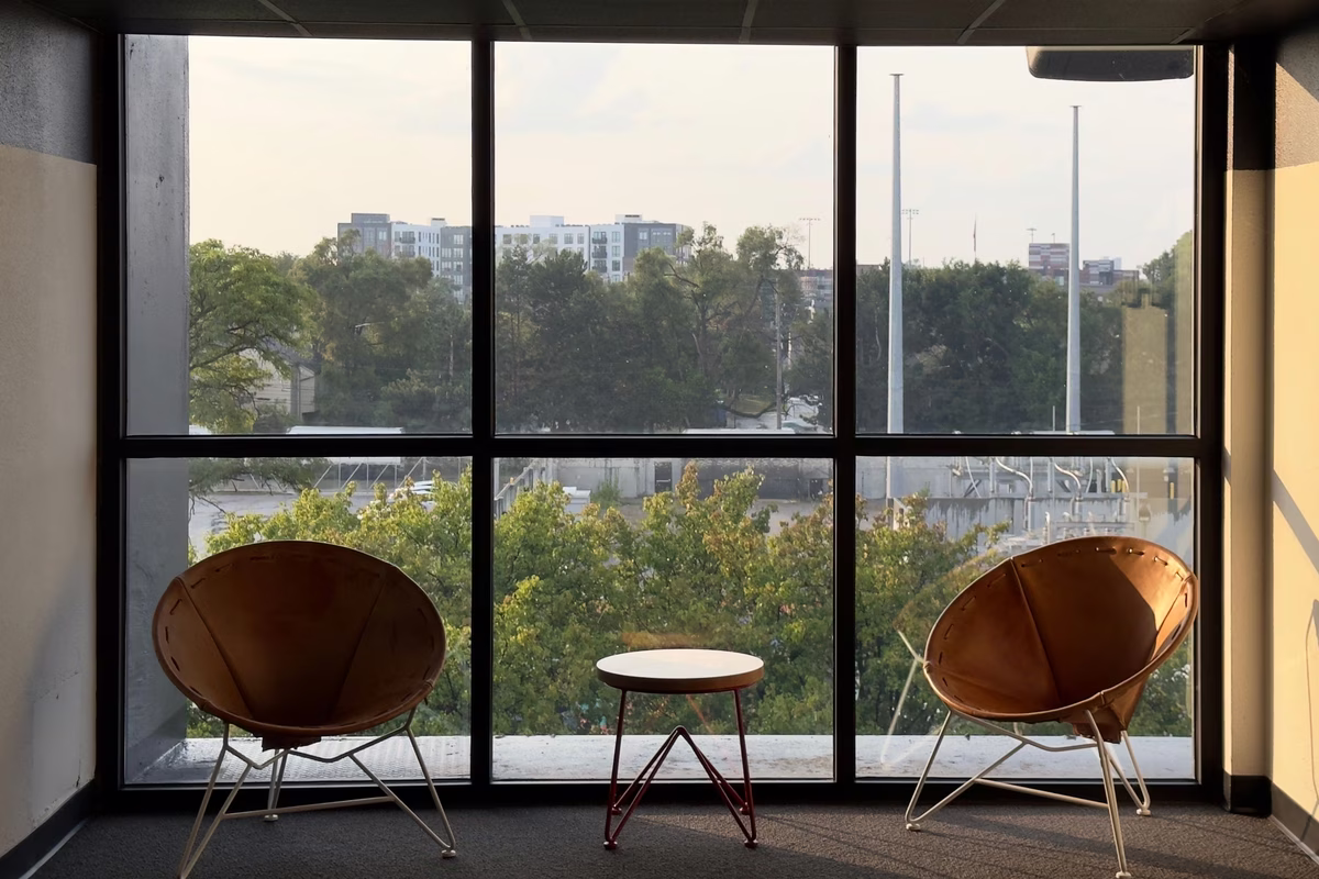 Two lounge chairs and a side table in a quiet corner beside office windows
