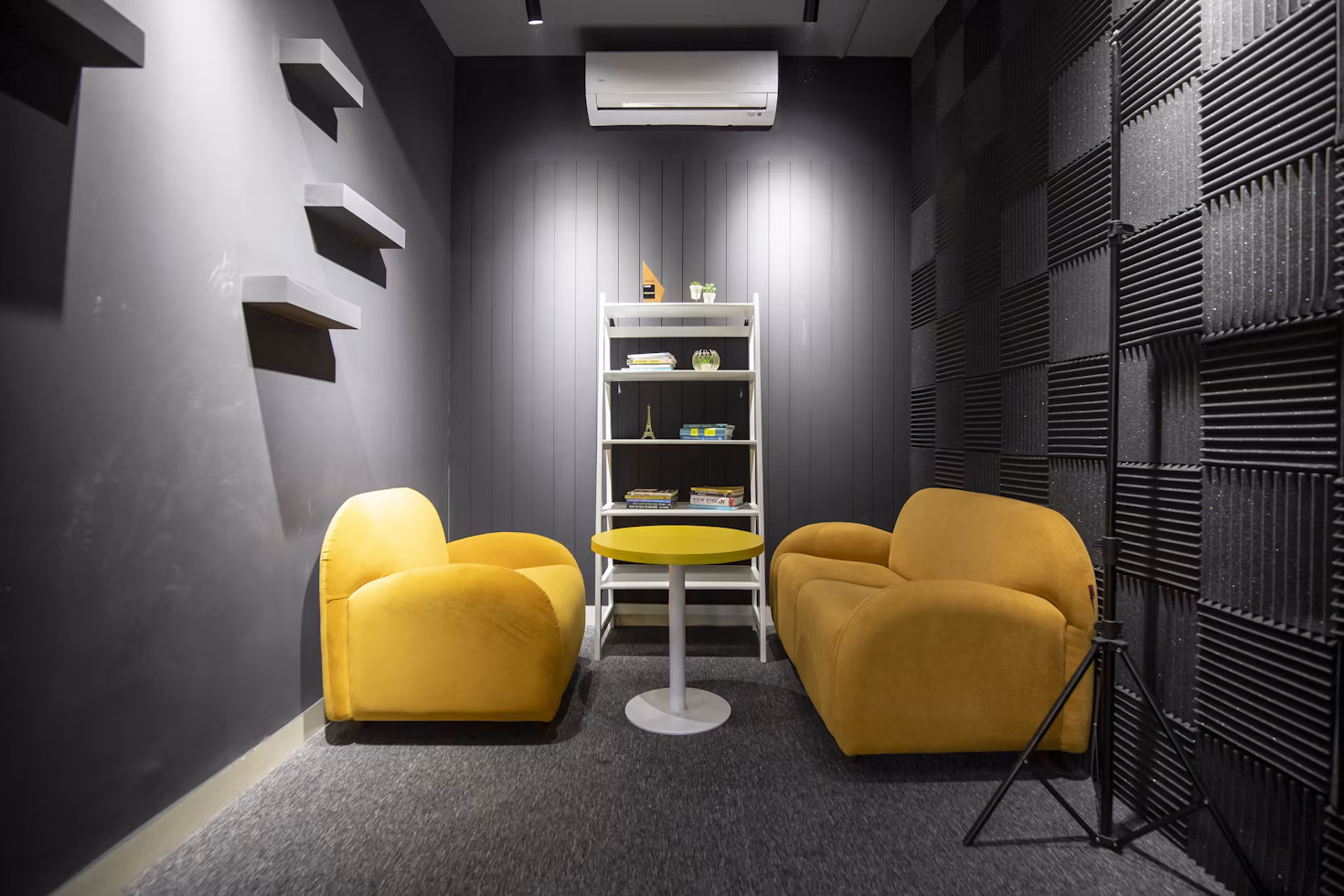 Black acoustic foam panels covering a wall in a small room with armchairs and a side table