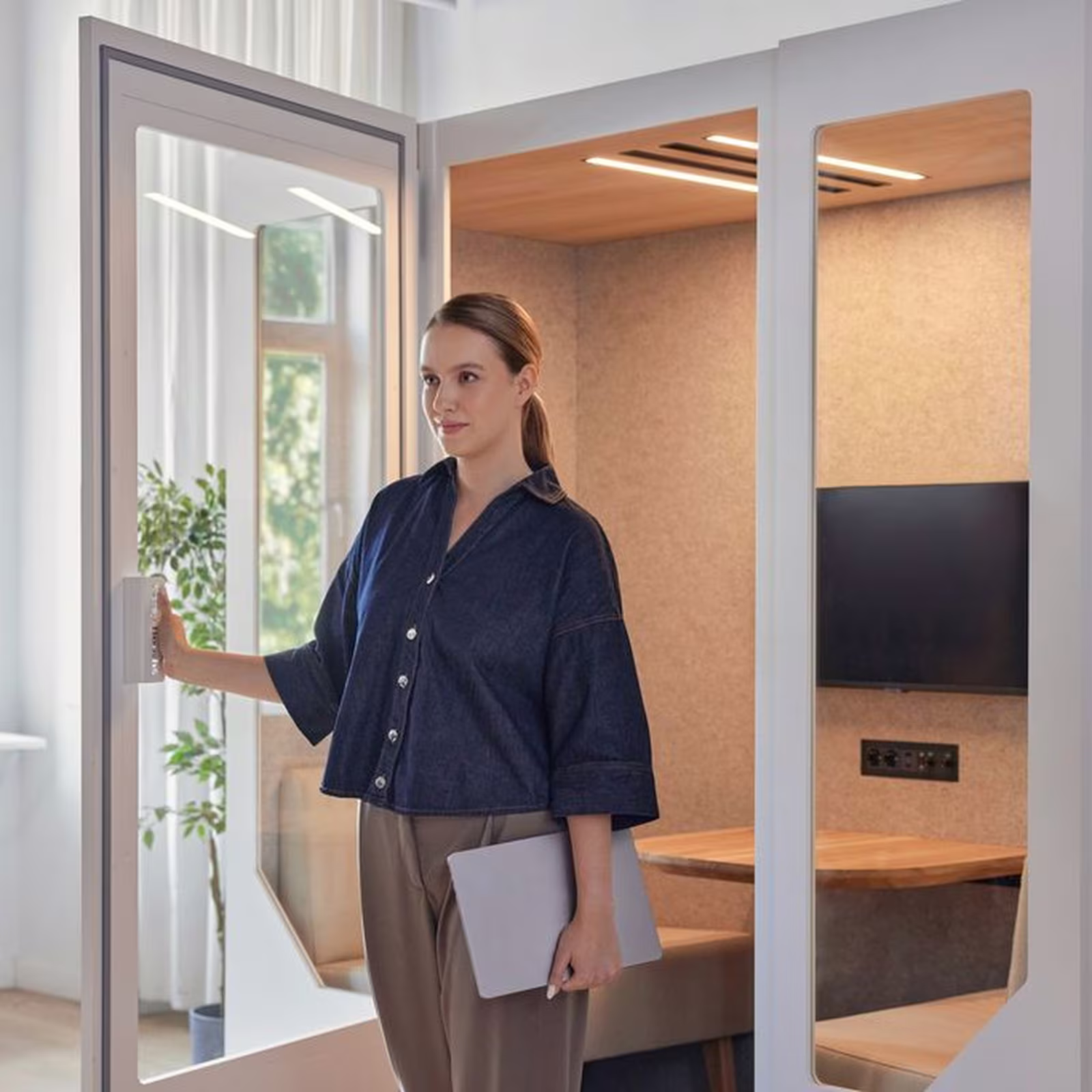 Woman entering a soundproof office booth with laptop in hand