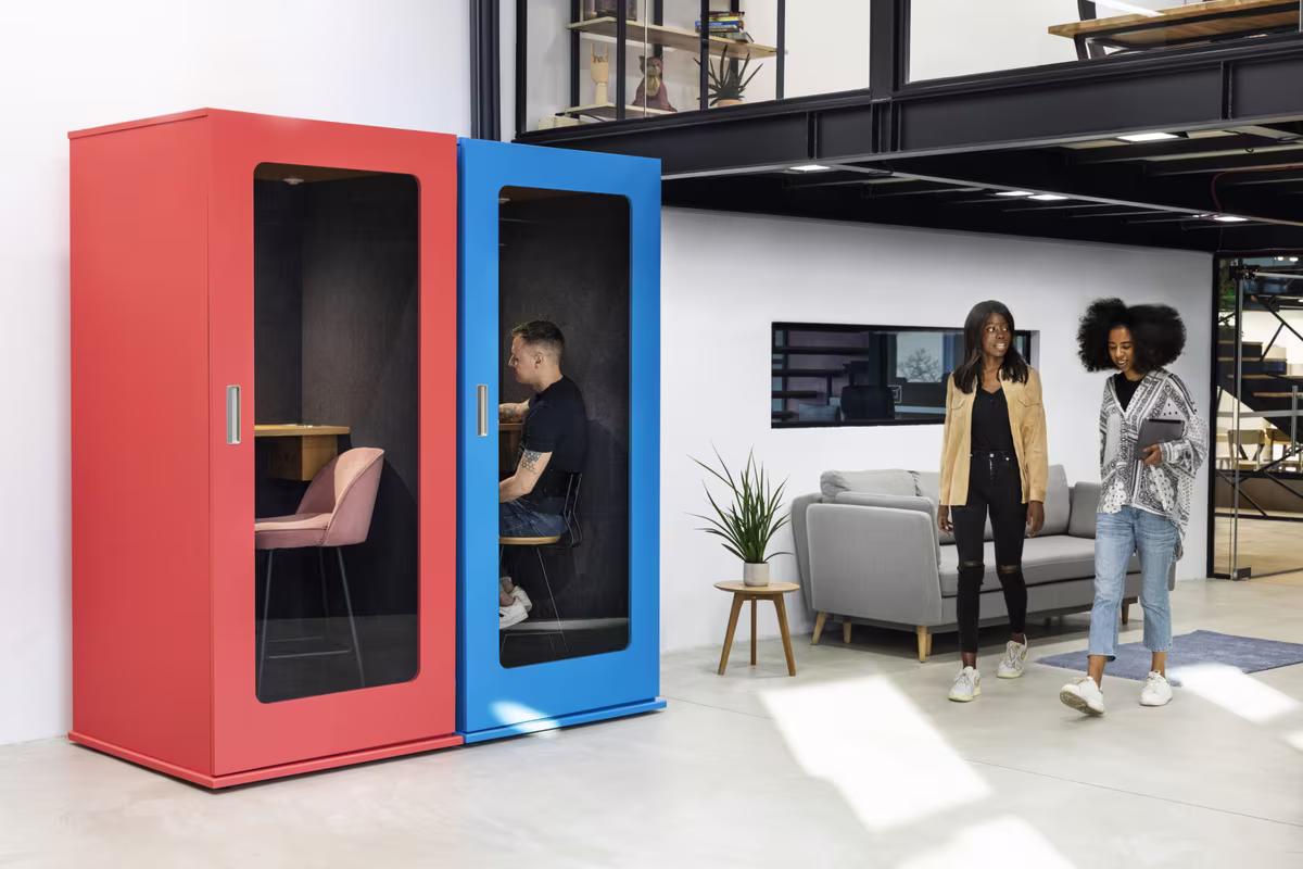 Man working inside a blue phone booth beside a red booth in a coworking space