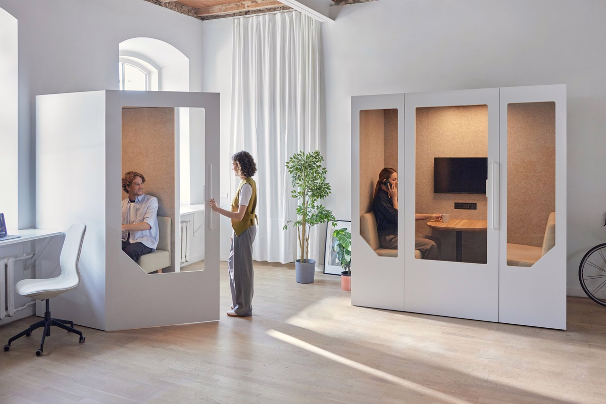 Modern office with white acoustic booths, featuring people using private work and meeting spaces in a bright, minimalist interior.
