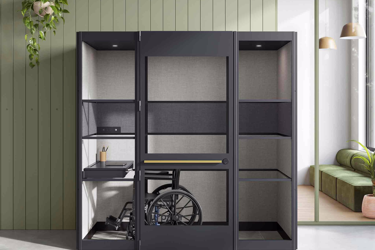 Wheelchair-accessible black office booth with a wheelchair parked inside, in front of a sage-green wall.