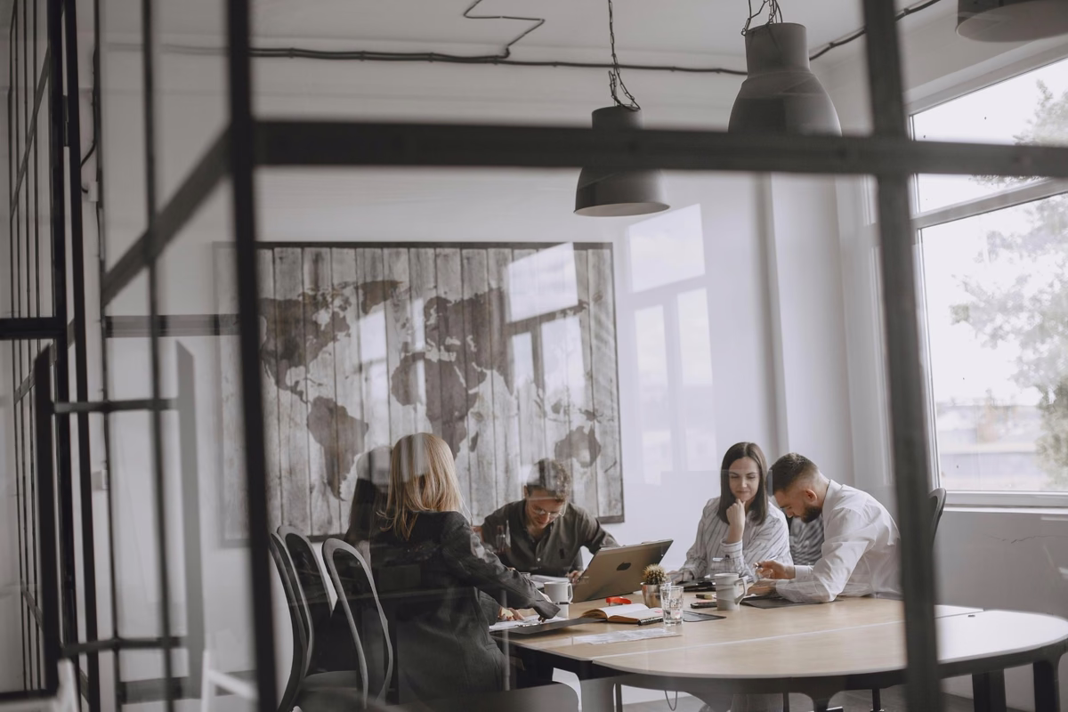 Team of professionals collaborating around a conference table in a modern glass-walled meeting room.