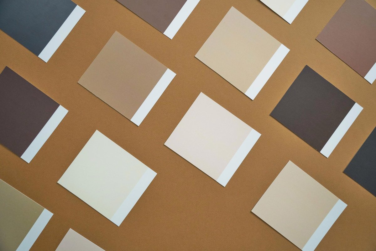 Neutral color palette samples in beige, cream, brown and grey arranged diagonally on a warm brown background.