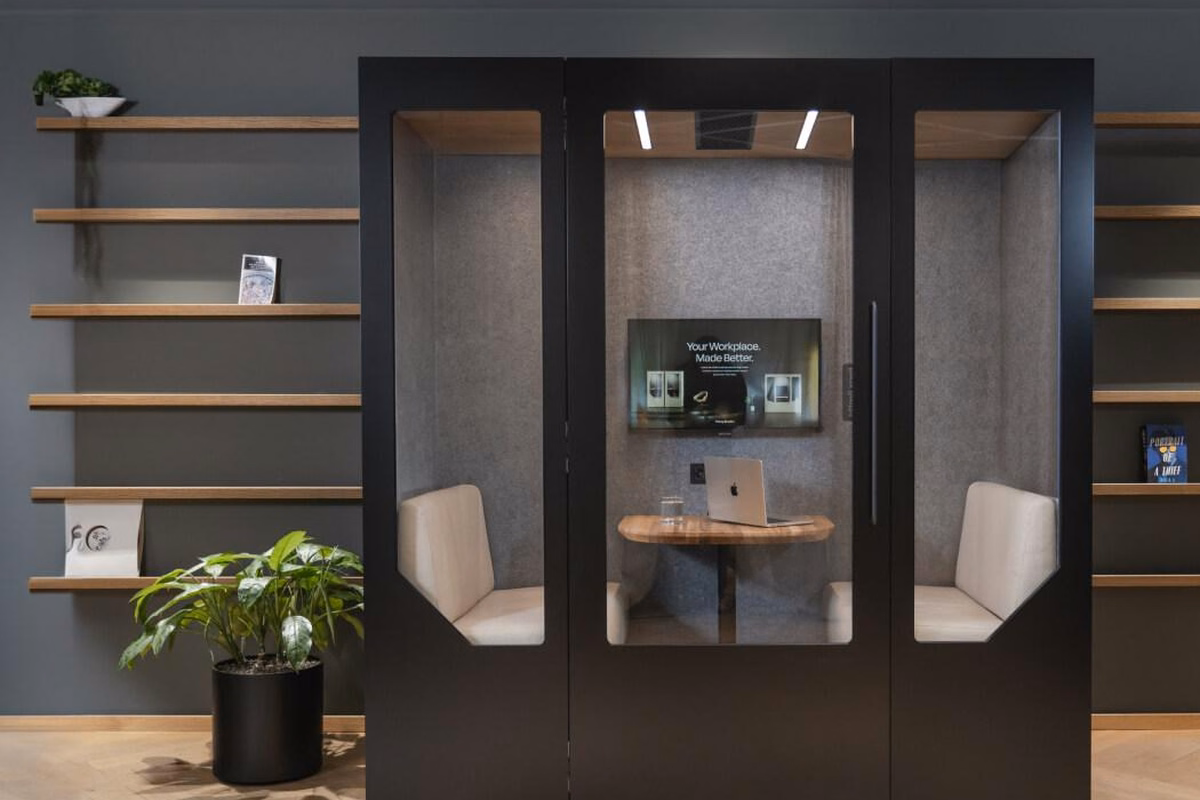 Modern black acoustic meeting booth with glass doors, comfortable seating, wooden table and integrated screen in a stylish office.