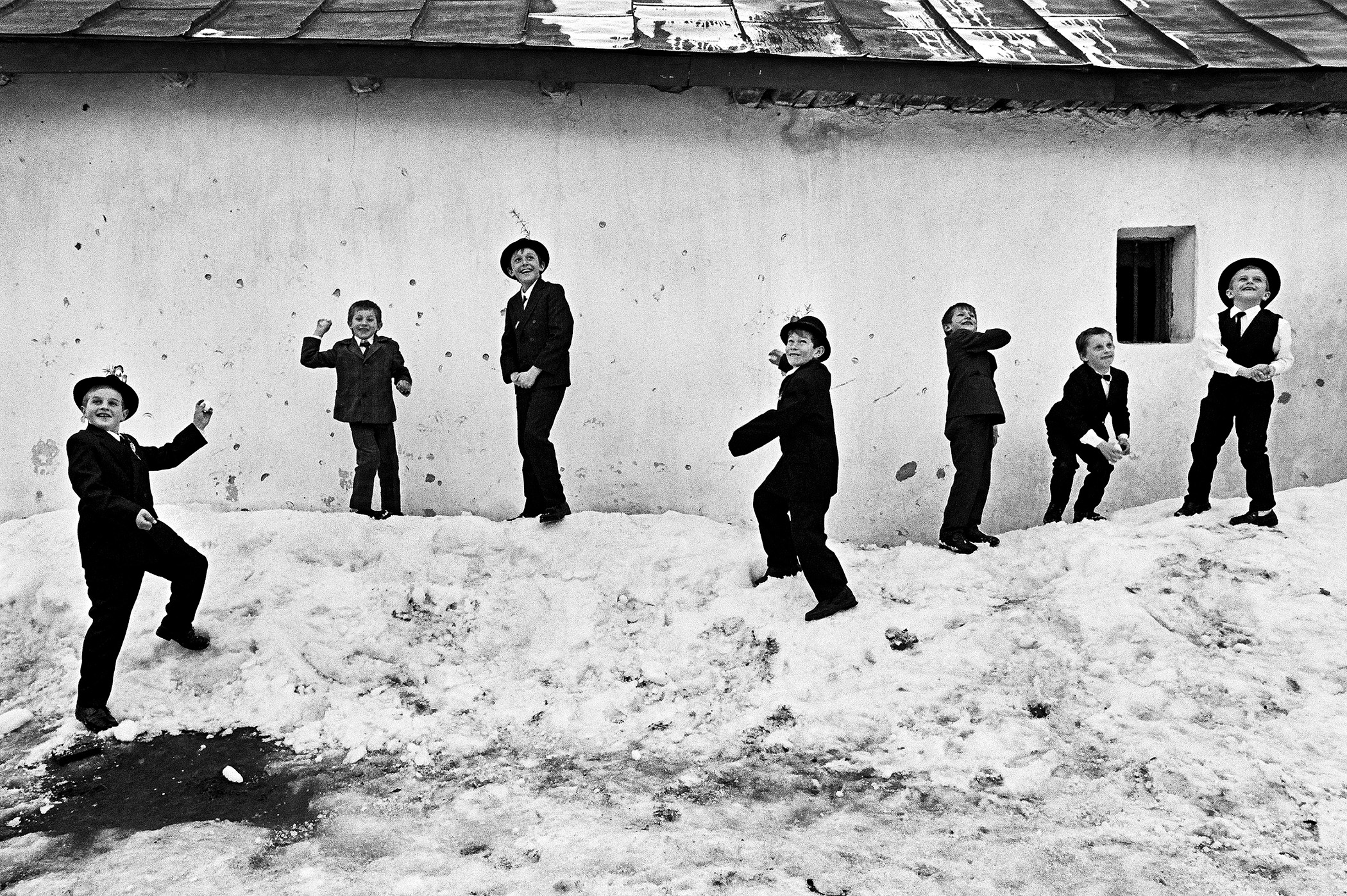 Sedm mladých kluků s úsměvy na tvářích hází sněhové koule po fotografovi v Rumunsku.