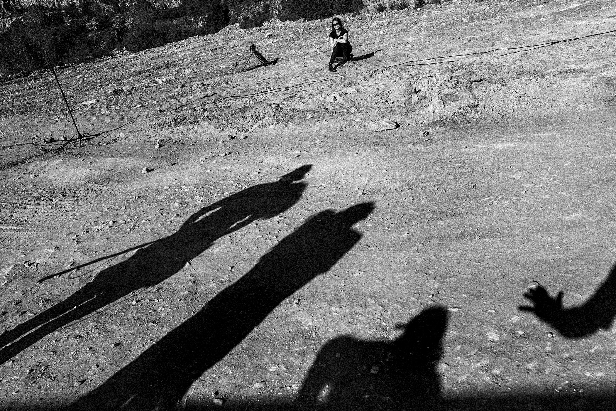 Na vyprahlé písčité zemi se promítají stíny osob, v pozadí sedí herečka z divadla Amerikánka