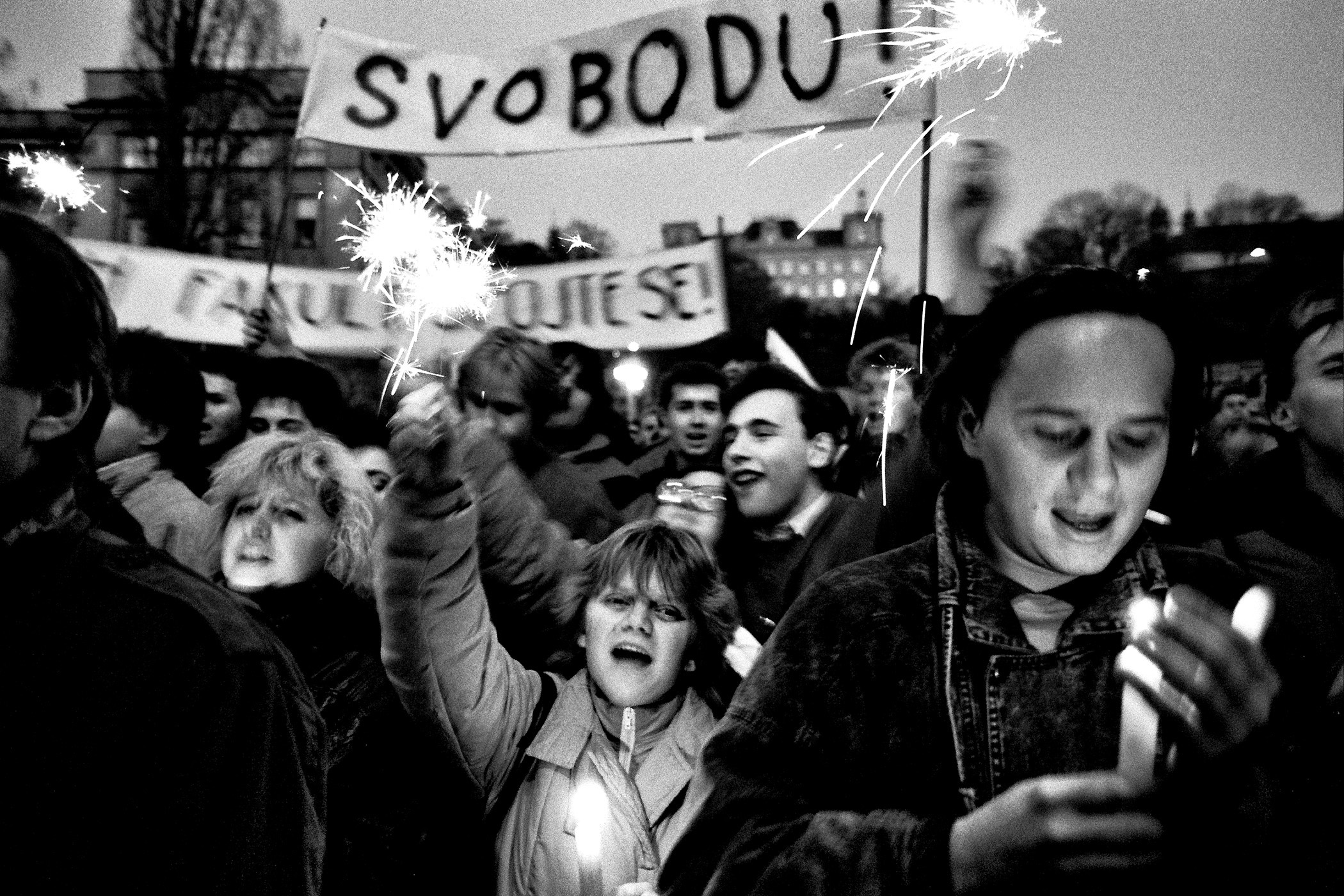 Skupina mladých lidí na protirežimní demonstraci. Lidé zapalují svíčky a nesou nápis SVOBODU!
