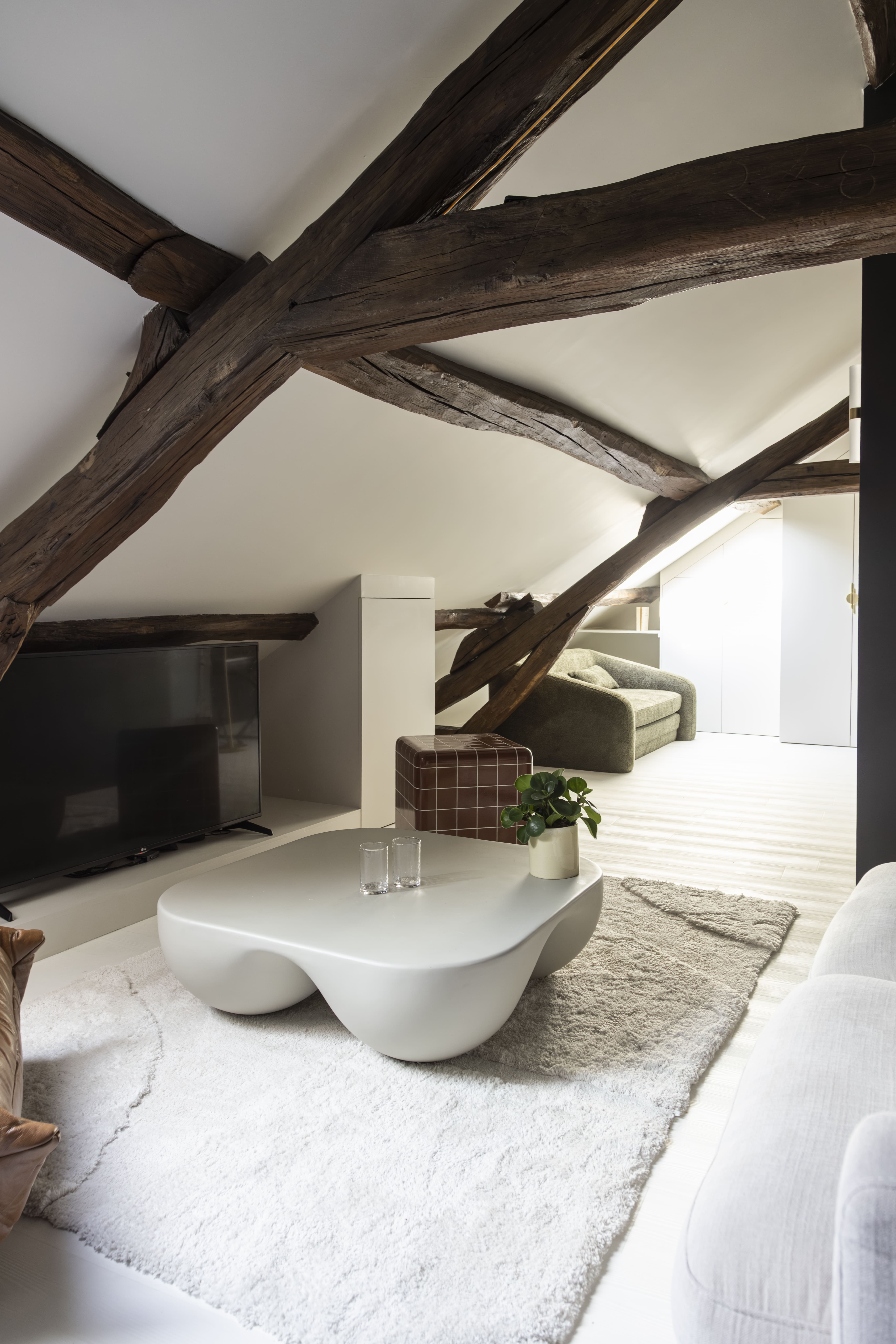 Chambre parentale sous combles avec poutres apparentes et teintes naturelles