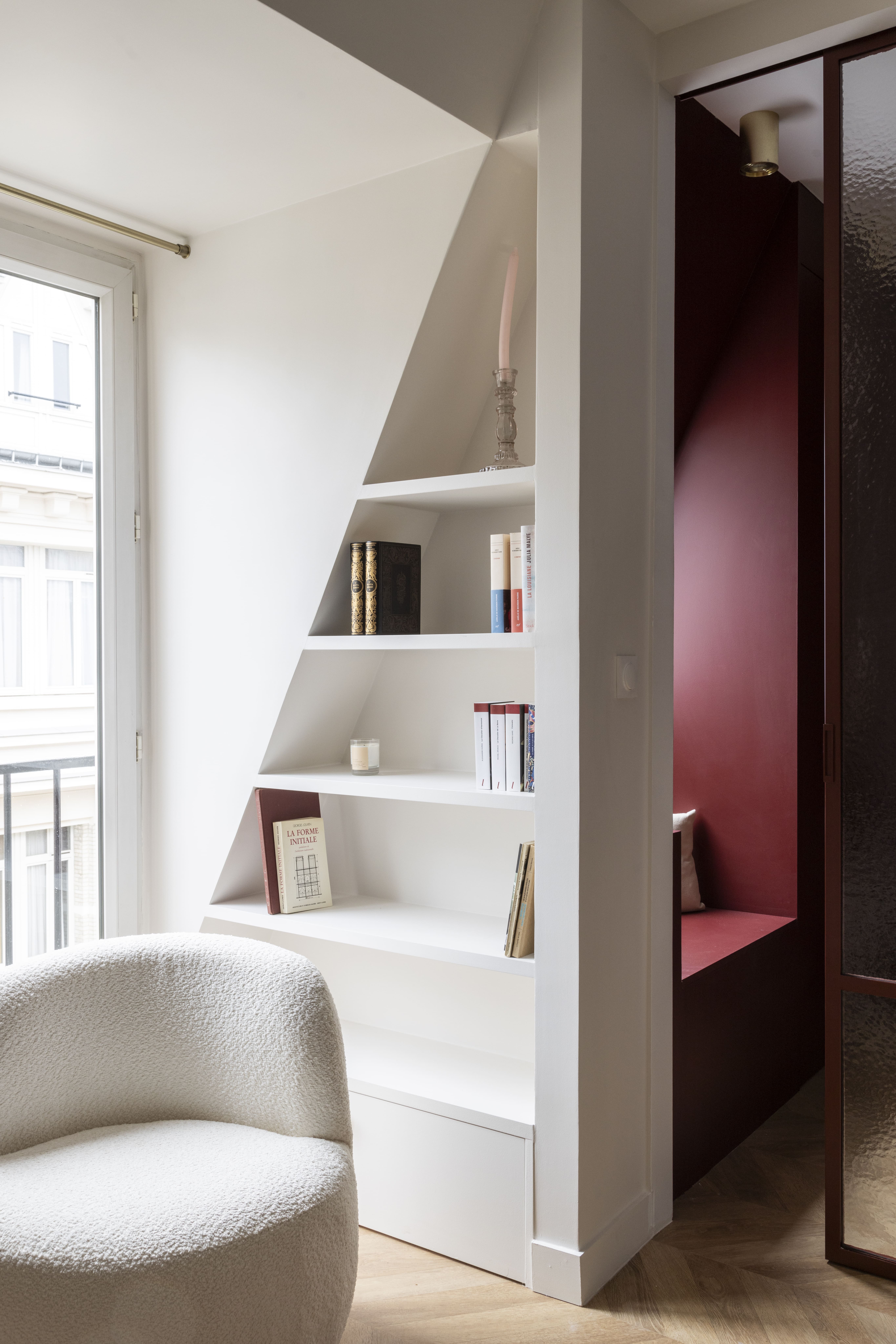 Coin lecture sous pente avec bibliothèque blanche et fauteuil arrondi – aménagement d’intérieur à Paris