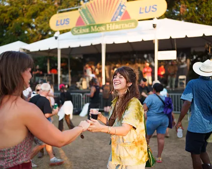Woman smiling and dancing with a drink at an outdoor music festival.