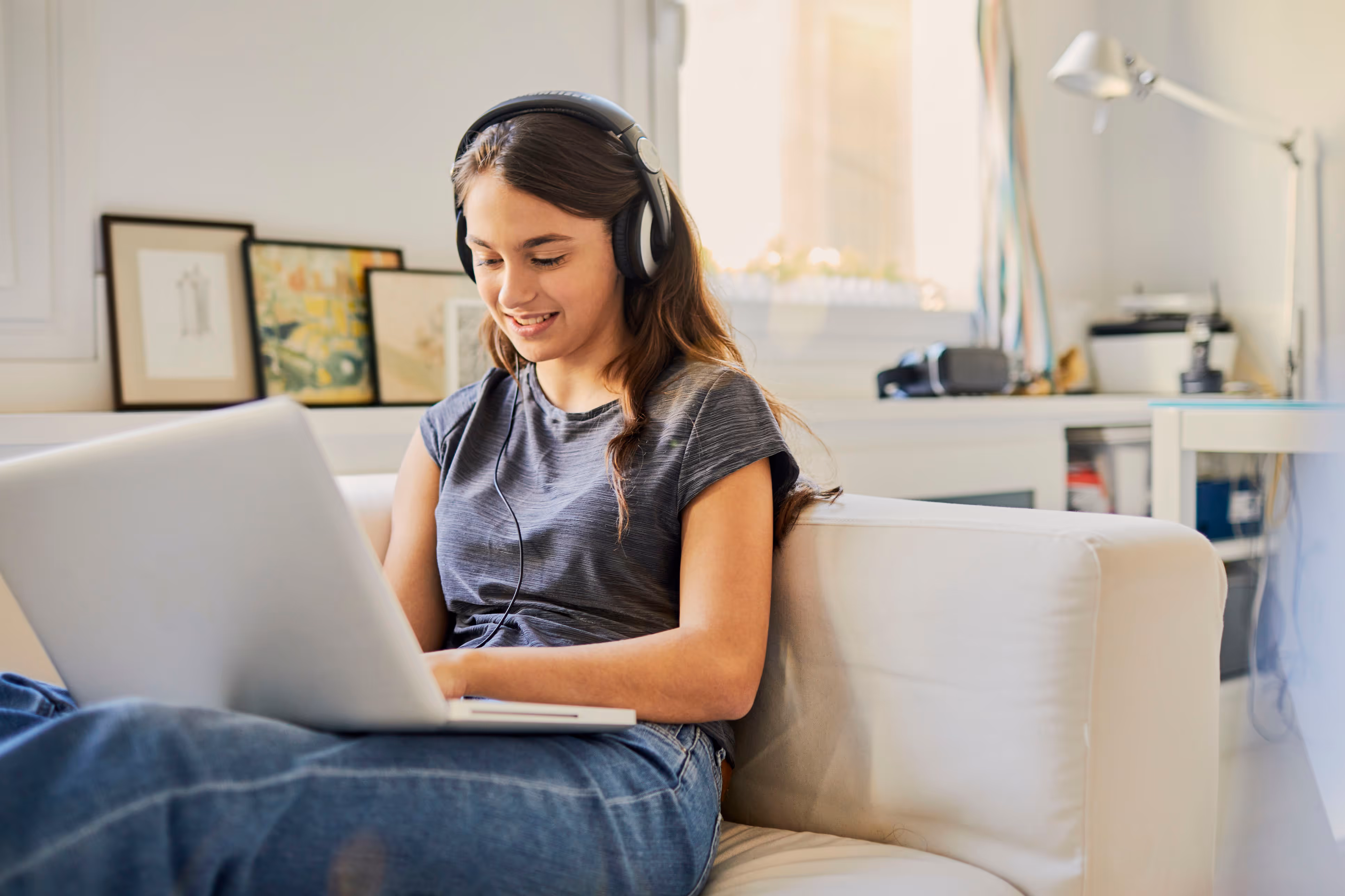 Teen using a laptop and headphones on a couch in her home.
