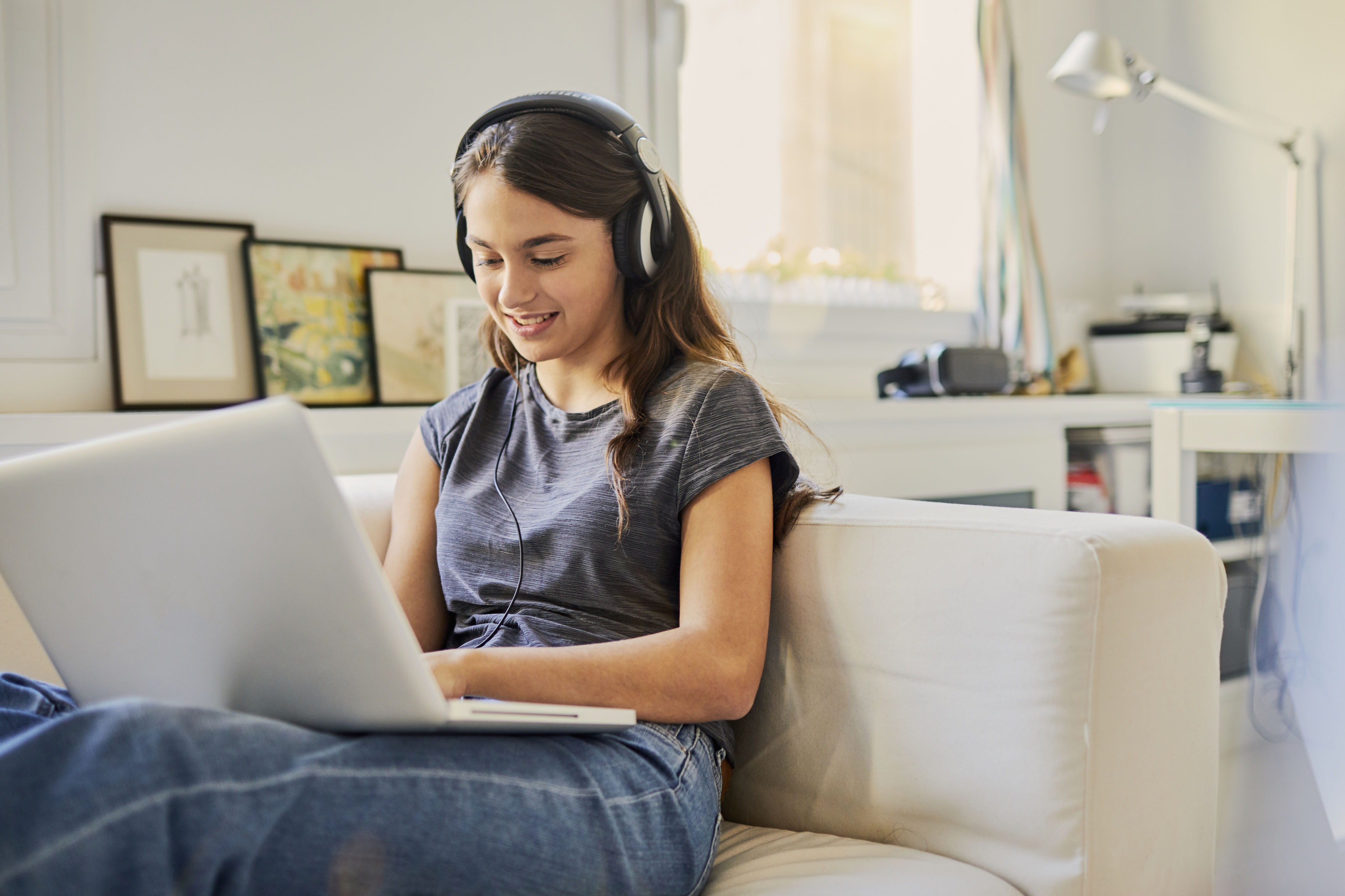 Teen using a laptop and headphones on a couch in her home.